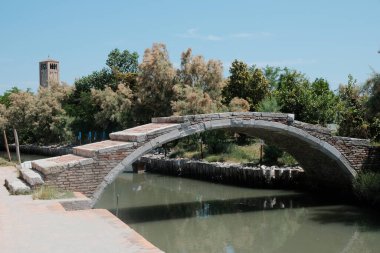 Akan bir nehir boyunca uzanan ve arka planda yüksek bir kulenin varlığıyla güçlendirilen güzel bir köprü var.