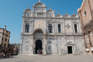 Büyük ve etkileyici beyaz bir bina dimdik ayakta duruyor, her şeyin üstünde parlak mavi gökyüzüne karşı katıksız bir tezat oluşturuyor.