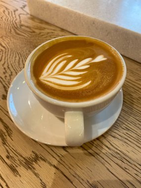 Bir fincan kapuçino ve ahşap masada güzel bir latte sanatı. Düz yatış stili. Düz beyaz. İçmeye hazır..