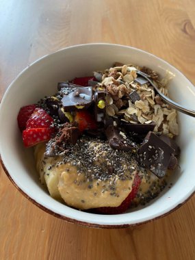 Tahta Masa üzerinde Chia Seeds, Muz, Çilek, Yuvarlak Yulaf ve Acı Çikolata parçaları olan protein kasesi. Yemeye hazır..