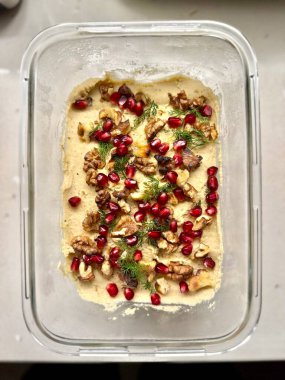 bowl of creamy hummus topped pomegranate seeds with chopped parsley and a drizzle of olive oil. The hummus is a light beige color and has a smooth texture. Homemade food clipart