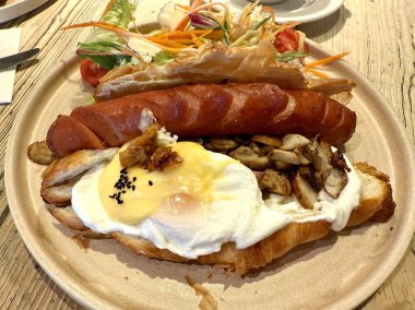 Kahvaltıda ahşap masa restoranında servis edilen sosisli ve haşlanmış yumurtalı kruvasan sandviçi.