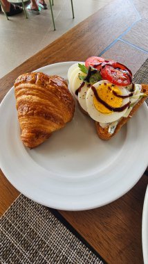 Kızarmış yumurta, salata yapraklı, ızgara mantarlı ve vişneli domatesli kruvasan sandviçli leziz kahvaltı.