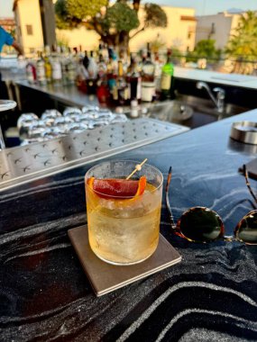 Zarif bir Negroni kokteyli, berrak bir buz küresi artı şık bir portakal kabuğu süslemesi. Kırsal ahşap bir zemin üzerinde mükemmel bir şekilde işlenmiş içecek. Karışım, lüks kokteyller ve bar temaları için ideal.