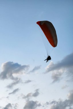 İki adamın siluetleri arka planda gökyüzüne karşı bir paraglider üzerinde uçuyor.