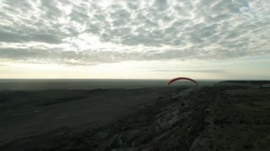 Kayaların ve tepelerin üzerinde bir yamaç paraşütünün üstündeki bir İHA üzerinde paraşüt üzerinde bir paraşütçü paraşütü üzerindeki video alanı 4k yatay video turuncu paraglider