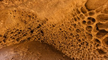 Doğal erozyon delikleri ve bal peteği desenleri ile kaplı bir kumtaşı duvar tafonisinin fotoğrafı. Kazakistan 'ın Mangystau bölgesinde çekilen bu jeolojik oluşum, bir çöl mağarasında veya kayalıklarda rüzgar ve su erozyonu etkilerini gösteriyor..