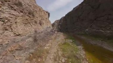 Mangystau, Kazakistan 'daki Zharmysh köyü yakınlarındaki dar ve kayalık bir kanyondan uçan FPV insansız hava aracı görüntüleri. Kanyon zemininde sarp kayalıklarla çevrili sığ bir dere var.. 