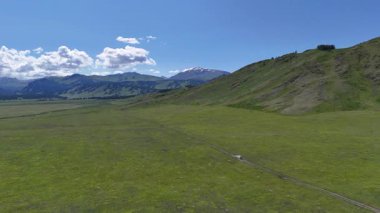 Bir yaz günü Doğu Kazakistan 'daki Eski Avusturya Yolu boyunca, uzak dağları olan bir vadide, yeşil bir tarladan geçen beyaz bir araba.