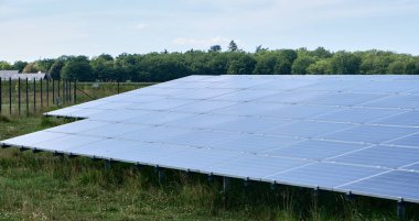Ağaçlar ve mavi gökyüzü olan kırsal bir alanda güneş enerjisi çiftliğinde güneş enerjisi çiftliği ve fotovoltaik paneller içeren büyük bir güneş enerjisi çiftliği. Doğayla uyum içinde yenilenebilir enerji üretimi.
