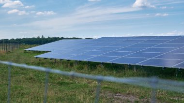 Ağaçlar ve mavi gökyüzü olan kırsal bir alanda güneş enerjisi çiftliğinde güneş enerjisi çiftliği ve fotovoltaik paneller içeren büyük bir güneş enerjisi çiftliği. Doğayla uyum içinde yenilenebilir enerji üretimi.