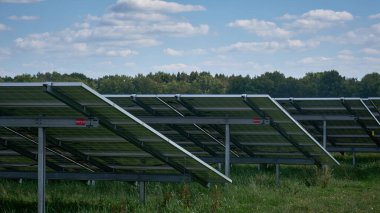 a large solar energy farm featuring rows of photovoltaic panels solar energy farm seen from behind, in a rural area with trees and blue skies. Renewable energy production in harmony with nature. clipart