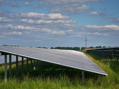 Ağaçlar ve mavi gökyüzü olan kırsal bir alanda güneş enerjisi çiftliğinde güneş enerjisi çiftliği ve fotovoltaik paneller içeren büyük bir güneş enerjisi çiftliği. Doğayla uyum içinde yenilenebilir enerji üretimi.