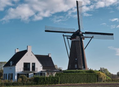 Nuenenenenen 'deki Korenmolen De Roosdock. Nuenen, Noord-Brabant' taki tarihi yel değirmeni manzarası. Modern ev, mavi gökyüzü ve yeşil manzara..