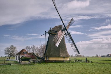 Historic drainage windmill Nijlannermolen near Workum in Friesland, Netherlands, surrounded by green fields and clouds on a bright day in March. clipart