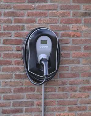 Kırmızı tuğladan bir duvara monte edilmiş elektrikli araç şarjı sürdürülebilir enerji çözümlerini ve büyüyen elektrikli araç altyapı eğilimini simgeliyor..