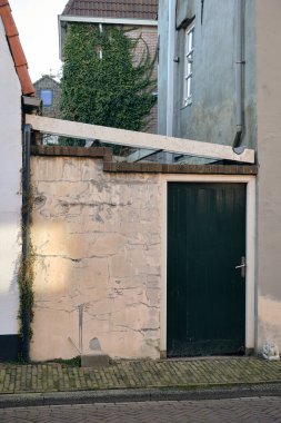 Hollanda, Kampen 'de yeşil kapılı, kaldırımlı ve her iki tarafında iki evi olan sarı alçı bir ara sokak cephesi..