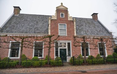 29 Aralık 2024 - Eelde / Hollanda: Eelde 'de yeniden inşa edilen Nijsinghhuis Portakalında yemyeşil bir bahçe, eğreltiotu, sarmaşık ve bulutlu bir kış ortamında gökyüzü altında tuğla bir duvar.