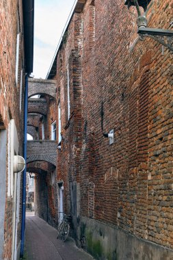 Hollanda, Kampen 'de, açık mavi gökyüzünün altında, kırmızı tuğlalı duvarları, kemerli yapısı ve klasik sokak lambası olan tarihi dar bir sokak..