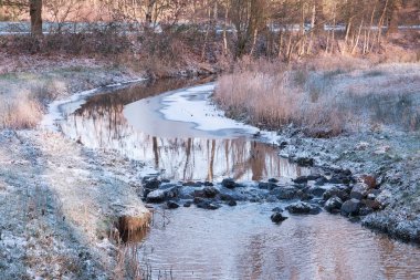 Drenthe, Hollanda: Buzlu çayırlar ve ağaçlarla çevrili kıvrımlı bir dere Hollanda kırsalında sakin bir kış manzarası yaratıyor.