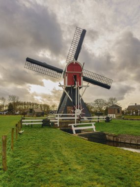 Historic Dutch hollow post mill, set in the green Utrecht countryside near Maarssen under a cloudy sky on a windy day. clipart