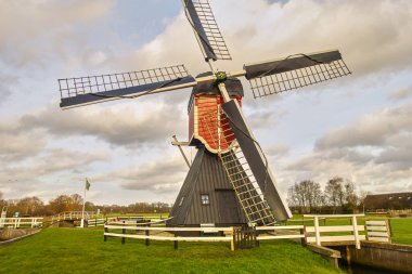 Historic Dutch hollow post mill, set in the green Utrecht countryside near Maarssen under a cloudy sky on a windy day. clipart