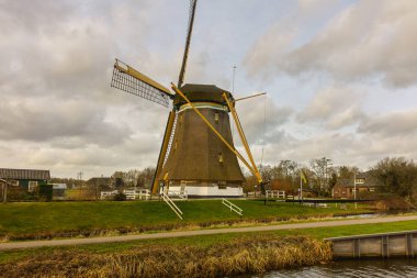 Hollanda 'nın tarihi yel değirmeni, Utrecht' in yeşil kırsalında Maarssen yakınlarında bulutlu bir gökyüzünün altında geçiyor..