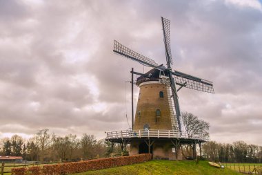 Hollanda 'nın Soest, Hollanda' da yeniden inşa edilen geleneksel yel değirmeni De Windhond, dramatik bulutlu bir gökyüzü altında yeşil çimenler ve çalılarla çevrili..