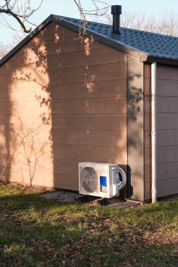 Outdoor heat pump unit installed against a vacation cottage at a holiday park, providing energy-efficient heating and cooling. clipart