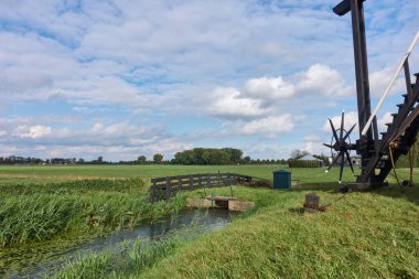 Hollanda 'nın Dussen, Noord Brabant, Hollanda' daki Noorthe Molen yel değirmenindeki manzara, ön planda küçük bir drenaj tesisi ve su yolu ile.