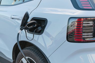 Modern bir yerleşim bölgesindeki bir kamu şarj istasyonunda çalışan beyaz elektrikli araba, sürdürülebilir kentsel hareketliliği vurguluyor.
