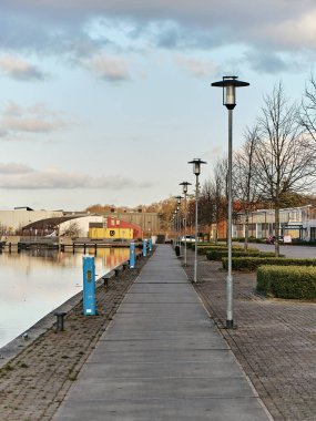 1 Mart 2025 - Assen Hollanda: Havenkwartier 'deki liman havzasında sakin su, sanayi binaları, beton oturma ve yumuşak akşam ışığı ile sakin liman.