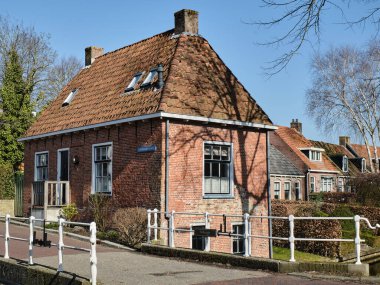 March 6, 2025: A scenic canal view in Dokkum, Friesland, with a bridge railing with the name Kloosterbrugje in the foreground and a row of historic workers' houses with gardens along the water. clipart