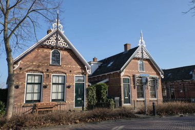 10 Mart 2025 - Grou, Hollanda: Köydeki ilk sosyal konutlardan biri olan 20. yüzyıl başlarında bir dizi işçi evi. Bu tuğla evlerde yatakhane pencereleri, siyah kiremitli çatılar ve klasik bir Hollanda tarzı var. Bir sıra budanmış ağaç sıralanır 