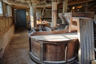 Tarihi bir değirmenin içinde ahşap kaplanmış geleneksel değirmen taşı. Ahşap dişliler ve şaftlar değirmen işlemini yürütüyor. Güneş ışığı, Bruchmuehle 'nin kırsal kesiminin eski kirişlerini ve işçiliğini vurgular