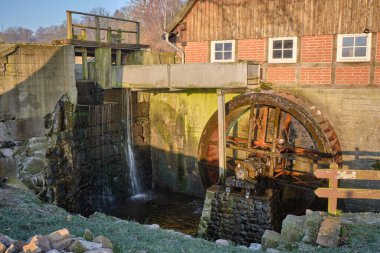 Sabah ışığında tarihi bir değirmenin su çarkını aştı. Çelik fabrikasının üzerinden akan su direksiyona güç veriyor. Değirmen, duvarlarında yosun olan bir tuğla ve kereste binasıdır..