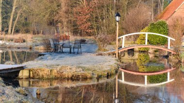 Bruchmuehle yansıtıcı değirmen gölet üzerinde küçük ahşap bir köprü, soğuk çimen, açık oturma ve yumuşak sabah ışığı sahne büyüten.