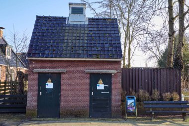 4 Mart 2025 - Tsjaard, Hollanda: Geleneksel bir saat, kemerli pencereler ve ağaç dalları tarafından çerçevelenmiş tarihi tuğla içeren tarihi kilise.