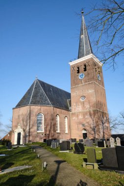 4 Mart 2025 - Tsjaard, Hollanda: Geleneksel bir saat, kemerli pencereler ve ağaç dalları tarafından çerçevelenmiş tarihi tuğla içeren tarihi kilise.