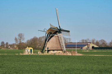 Tarihi Kimswerder Mill ve modern mandıra çiftliği, arka planda güneş panelleri, Friesland, Hollanda, kırsal bir alanda geçmiş ve geleceği harmanlıyor..