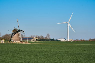 Tarihi Kimswerder Değirmeni ve parlak bir rüzgar türbini Hollanda, Friesland 'da yan yana duruyor. Kırsal bir bölgede geçmiş ve geleceği harmanlıyorlar..