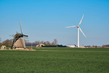 Tarihi Kimswerder Değirmeni ve parlak bir rüzgar türbini Hollanda, Friesland 'da yan yana duruyor. Kırsal bir bölgede geçmiş ve geleceği harmanlıyorlar..