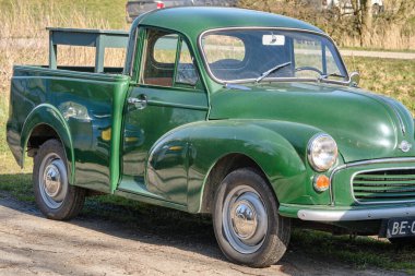 7 Mart 2025 - Ezumazijl-Hollanda: Güneşli bir günde güneşli bir köyde park etmiş, doğal elementlerle çevrili, küçük Morris marka klasik bir kamyonet.