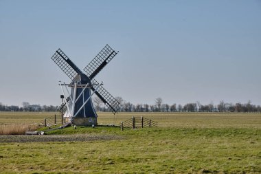 7 Mart 2025 - Ezumazijl-Hollanda: Friesland 'ın açık kırsal kesiminde geniş yeşil çayırlarla çevrili, uzun süre durgun kalan küçük geleneksel polder değirmeni De Gans.