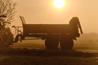 Traktör sabah sisi içinde Wormer, Low Holland 'ın düzlüklerinde yükselen güneşle siluetlendi. Altın bir tarım arazisi sabahın erken saatlerinde yıkandı..