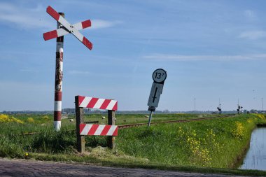 15 Nisan 2025 - Oostwoud-Hollanda: Kırsal kesimde tarihi Hoorn-Medemblik buhar tramvayı tarafından kullanılan korumasız demiryolu geçidine açık tabela ve ilkbahar kır çiçekleriyle bakınız.