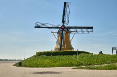 Sint-Philipsland-Hollanda: Rüzgâr değirmeni De Hoop, güneşli bir bahar gününde açık mavi bir gökyüzünün altında gelgit limanına bakan çimenli bir hendeğin üzerinde dimdik duruyor.
