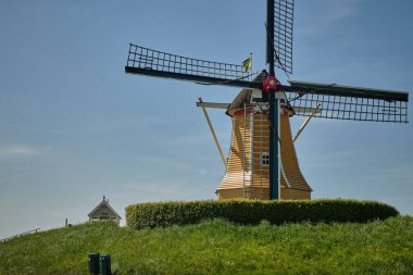 Sint-Philipsland-Hollanda: Rüzgâr değirmeni De Hoop, güneşli bir bahar gününde açık mavi bir gökyüzünün altında gelgit limanına bakan çimenli bir hendeğin üzerinde dimdik duruyor.