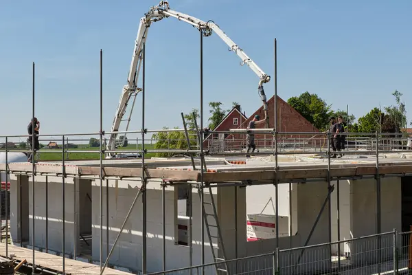 30 Nisan 2025 - Stavenisse-Hollanda: İşçiler açık mavi gökyüzü altında yeşil tarlalarla çevrili bir Hollanda köyündeki bir inşaat alanında pompa kamyonuyla zemine beton döküyorlar.