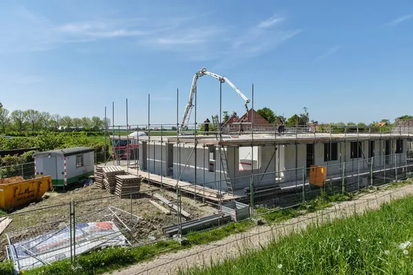 30 Nisan 2025 - Stavenisse-Hollanda: İşçiler açık mavi gökyüzü altında yeşil tarlalarla çevrili bir Hollanda köyündeki bir inşaat alanında pompa kamyonuyla zemine beton döküyorlar.